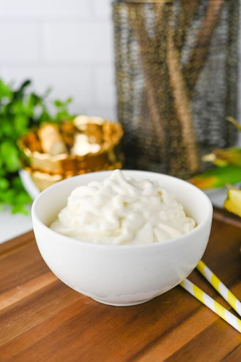 A bowl of homemade Dole Whip with a creamy soft-serve texture sits on a wooden serving board. The Disney-inspired pineapple dessert is swirled into the bowl and served immediately after blending, creating a smooth, light, and refreshing frozen treat perfect for warm weather.