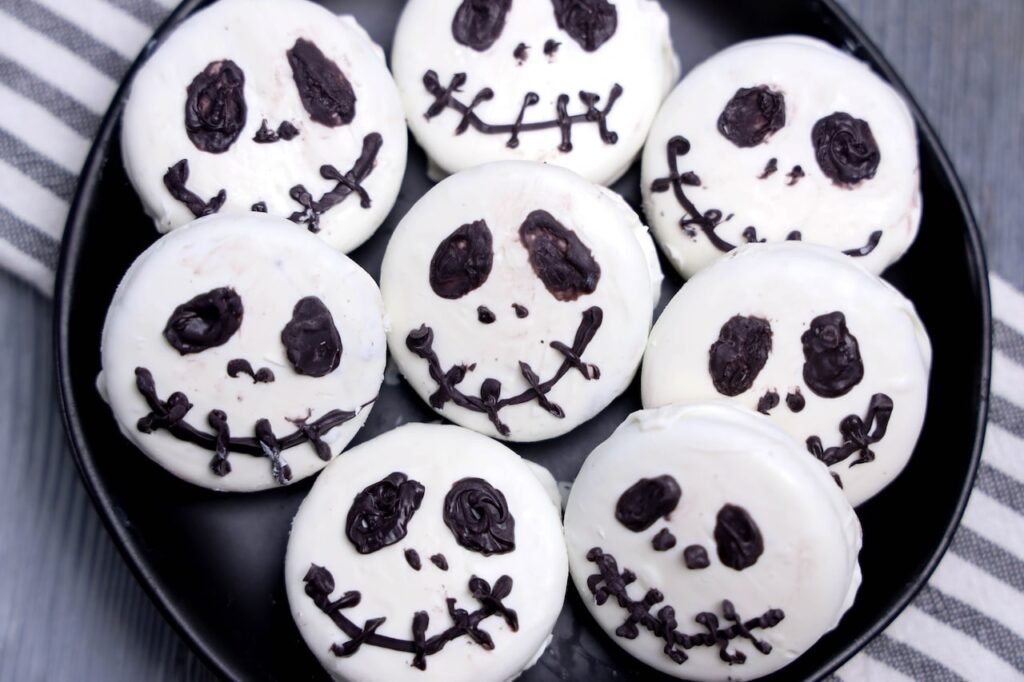 Close-up view of homemade Jack Skellington Oreos arranged on a black serving plate. The Oreo cookies are coated in white candy melts and decorated with black candy melts to create Jack Skellington's iconic eyes, nose, and stitched smile. This finished Halloween dessert is inspired by The Nightmare Before Christmas and is ready to serve for parties, movie nights, or spooky season gatherings.