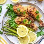 Cooked lemon herb air fryer chicken legs served on a plate with roasted asparagus, fresh parsley, lemon slices, and lemon zest. The chicken has golden, crispy skin and is garnished with fresh herbs. This image shows the finished recipe ready to serve.