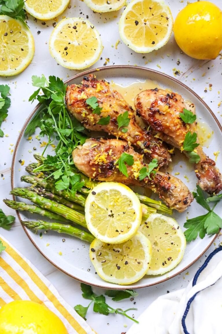 Cooked lemon herb air fryer chicken legs served on a plate with roasted asparagus, fresh parsley, lemon slices, and lemon zest. The chicken has golden, crispy skin and is garnished with fresh herbs. This image shows the finished recipe ready to serve.