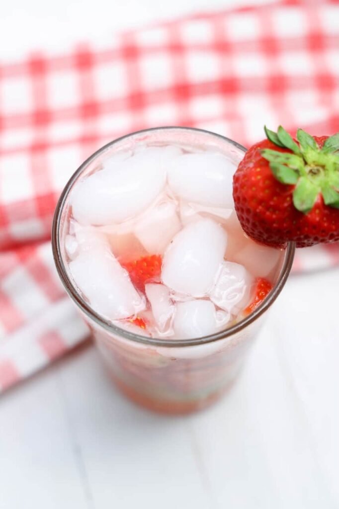 Top view of strawberry basil lemonade filled with ice and fresh strawberries with a strawberry garnish on the rim of the glass.