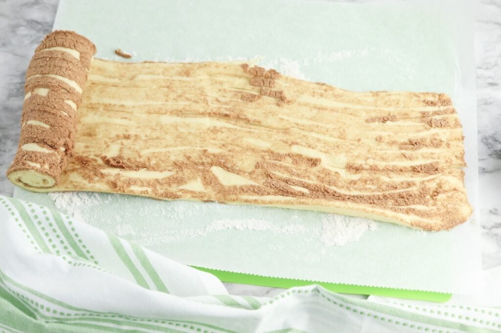 Pillsbury cinnamon roll dough unrolled into one long sheet on floured parchment paper, showing the cinnamon filling swirled throughout the dough before adding the brownie batter.